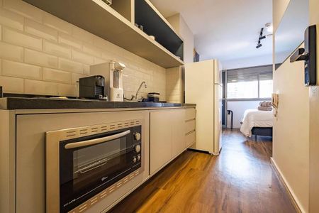 Cozinha com geladeira, fogão e microondas, com móveis brancos e azuis, e piso de madeira. de kitnet/studio à venda com 1 quarto, 26m² em Pinheiros, São Paulo