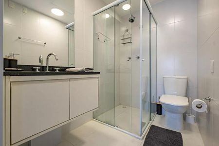 Banheiro com piso de porcelanato, pia de granito e chuveiro de vidro. de kitnet/studio à venda com 1 quarto, 26m² em Pinheiros, São Paulo