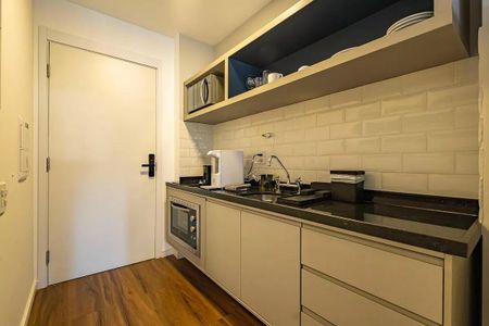 Cozinha com móveis brancos e armários de cor escura, com piso de madeira e bancada de granito. de kitnet/studio à venda com 1 quarto, 26m² em Pinheiros, São Paulo