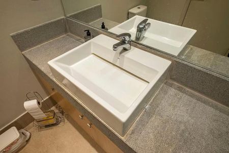 Studio à venda com 31m², 2 quartos e 1 vagaBanheiro com pia e espelho, com uma superfície de granito e um chão de porcelanato.