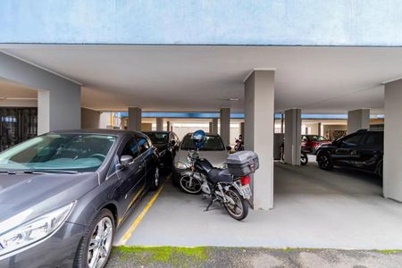 Apartamento à venda com 84m², 3 quartos e 2 vagasPatio de garagem com vários carros e motos estacionados, com uma parede branca e colunas de concreto.