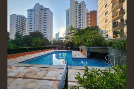 Apartamento à venda com 344m², 6 quartos e 4 vagasPiscina com fundo azul e borda branca, cercada por plantas e edifícios de apartamentos ao fundo.