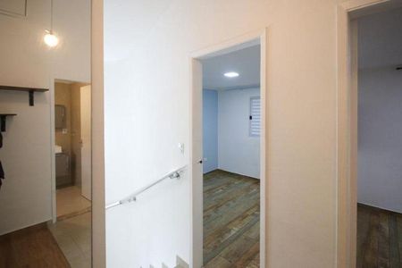 Casa à venda com 150m², 2 quartos e 1 vagaParede branca e corredor com escada e corrimão de metal, iluminado por lâmpada de parede.