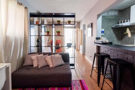 Sala de estar com sofá, mesa e estante de madeira, iluminada por luz natural e artificial. de apartamento à venda com 2 quartos, 35m² em Jardim Paulista, São Paulo