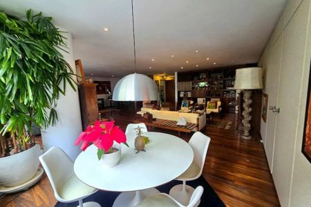 Apartamento à venda com 370m², 6 quartos e 3 vagas Apartamento à venda com 370m², 6 quartos e 3 vagasSala de estar com mesa redonda e cadeiras brancas, pinoquinha e planta vermelha, iluminação branca e madeira escura no chão.