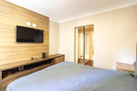 Quarto com cama, TV e móveis de madeira, com uma porta de vidro para o banheiro. de apartamento à venda com 2 quartos, 109m² em Jardim Paulista, São Paulo
