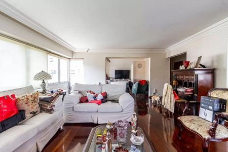 Apartamento à venda com 260m², 6 quartos e 3 vagasSala com sofás brancos, móveis de madeira e decoração em tons de vermelho e branco.