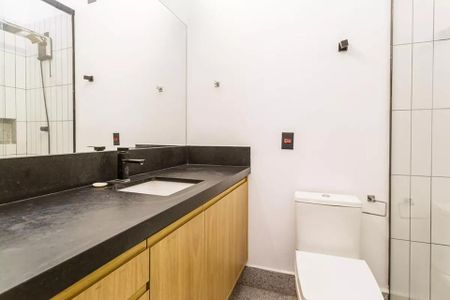 Banheiro com pia e vaso sanitário em madeira e pedra preta, com espelho e chuveiro. de casa à venda com 2 quartos, 100m² em Moema, São Paulo
