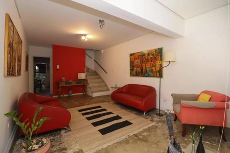 Sala com dois sofás vermelhos, uma mesa e uma escada, com uma pintura na parede e uma planta no chão. de casa à venda com 2 quartos, 110m² em Perdizes, São Paulo
