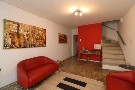 Sala com móveis vermelhos e quadros de arte em estilo cubista, com uma escada em madeira e uma mesa de madeira no fundo. de casa à venda com 2 quartos, 110m² em Perdizes, São Paulo