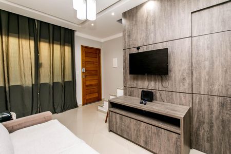 Sala de estar com sofá branco e TV montada na parede, com uma porta de madeira na fundo. de casa à venda com 2 quartos, 74m² em Vila Santa Edwiges, São Paulo