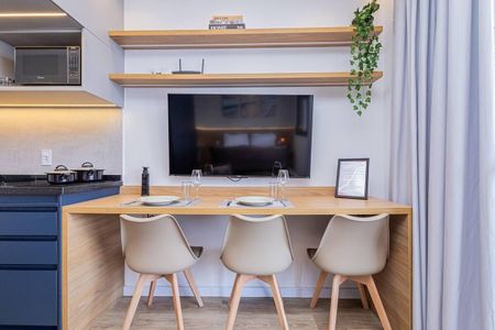 Apartamento à venda com 27m², 1 quarto e 1 vagaCozinha com mesa de madeira e três cadeiras brancas, com pratos e copos sobre a mesa, e uma TV na parede.